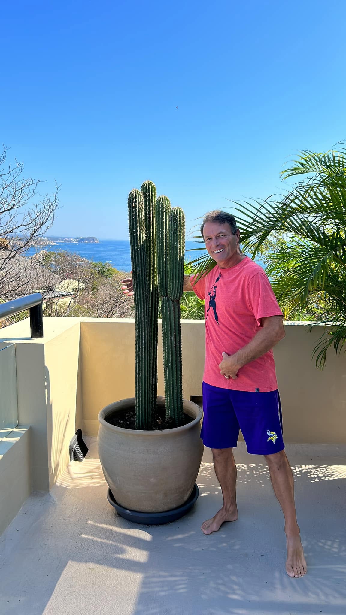 Cliente de El Edén junto a un cactus cardón en maceta de barro con vista al mar